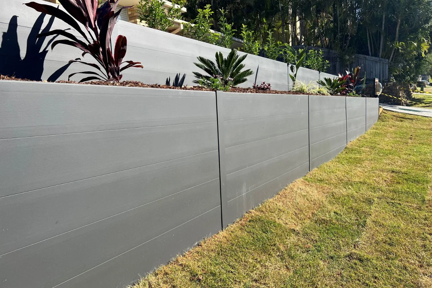 Concrete sleeper retaining wall with tropical garden bed planting along a driveway