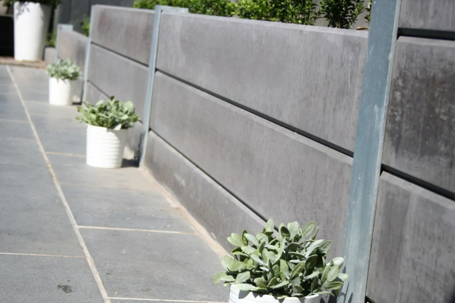 Concrete sleeper retaining wall with potted plants along a paved path