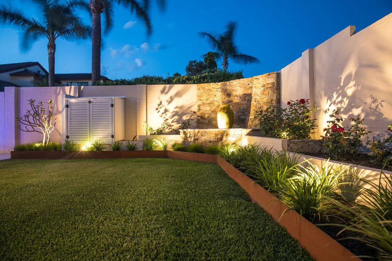 Stone-clad retaining wall with raised garden bed and steel edging, lit at night