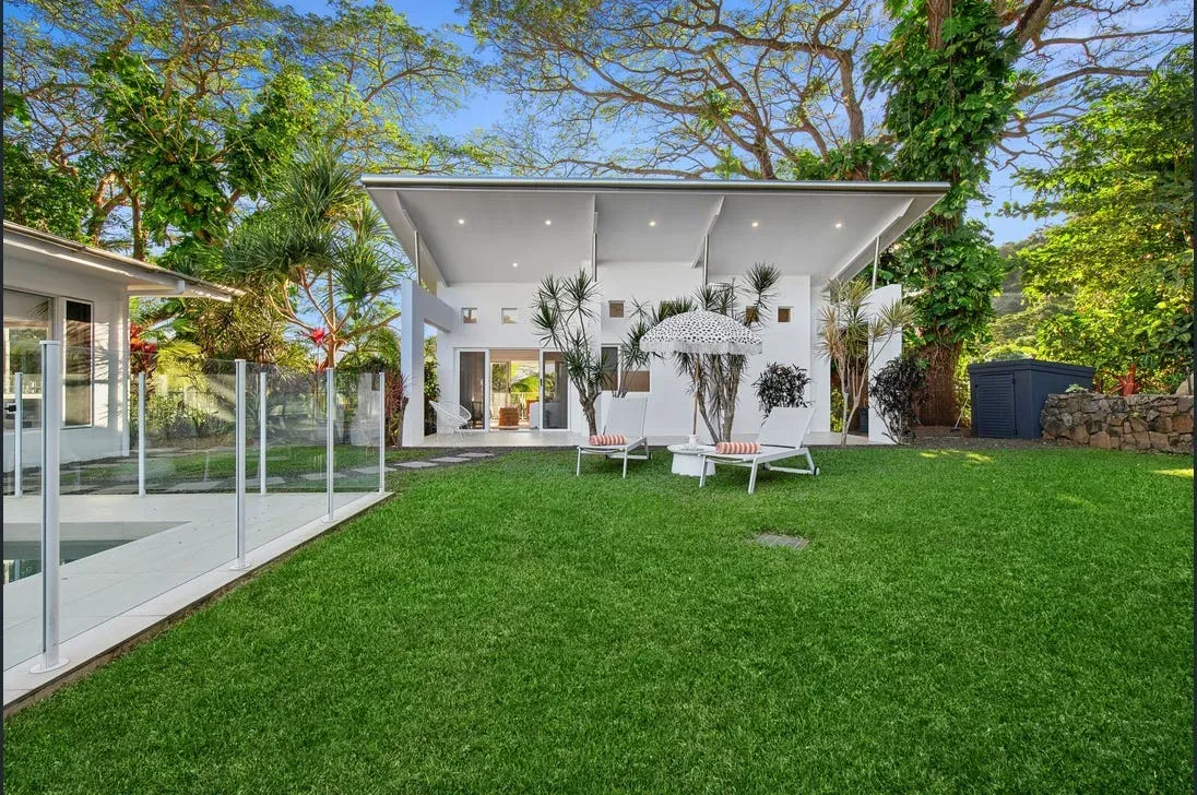 Backyard lawn with a glass-fenced pool and palm planting
